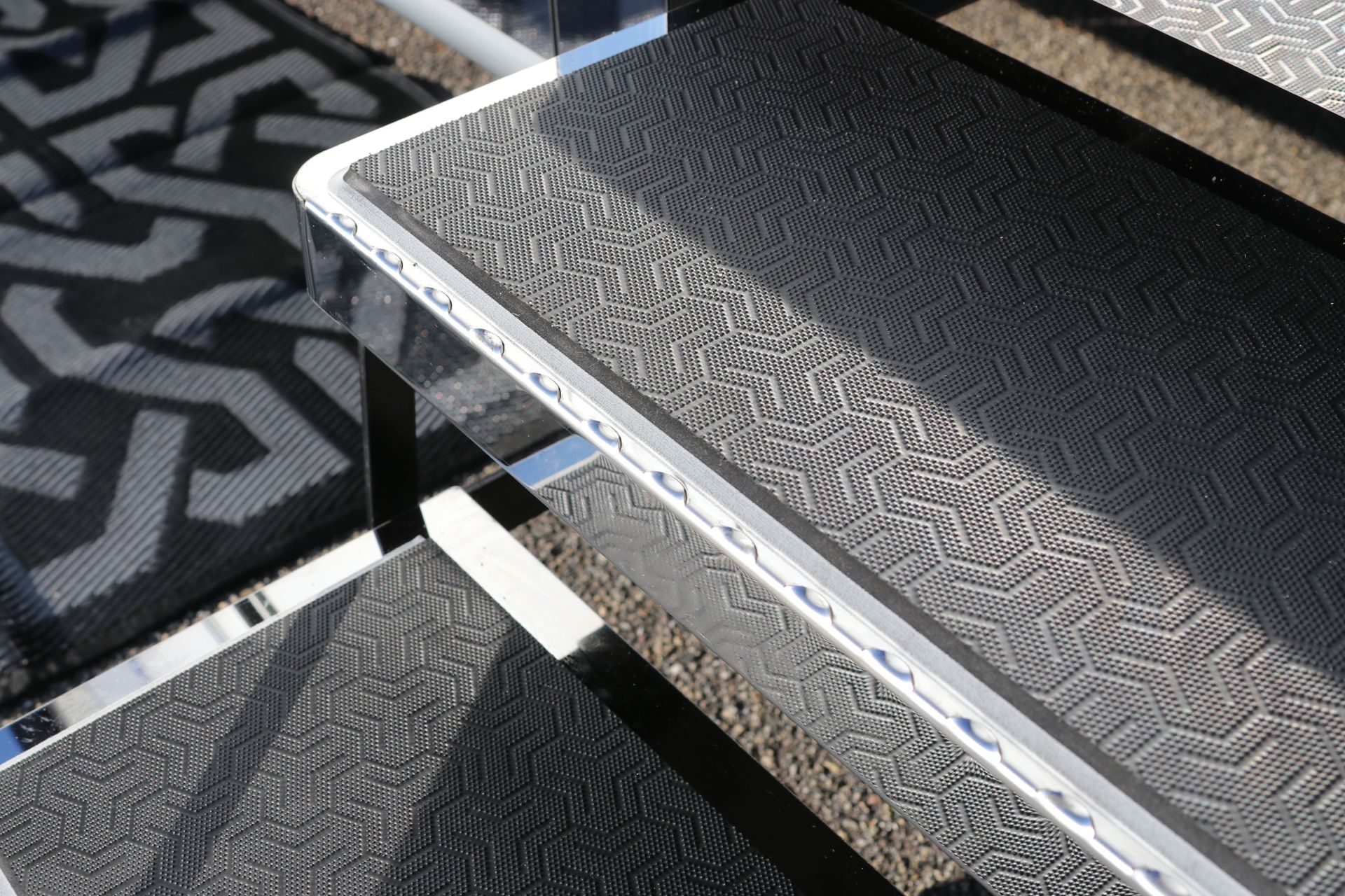 Close-up of three black steps with textured surfaces and metal trim, next to a patterned rug.