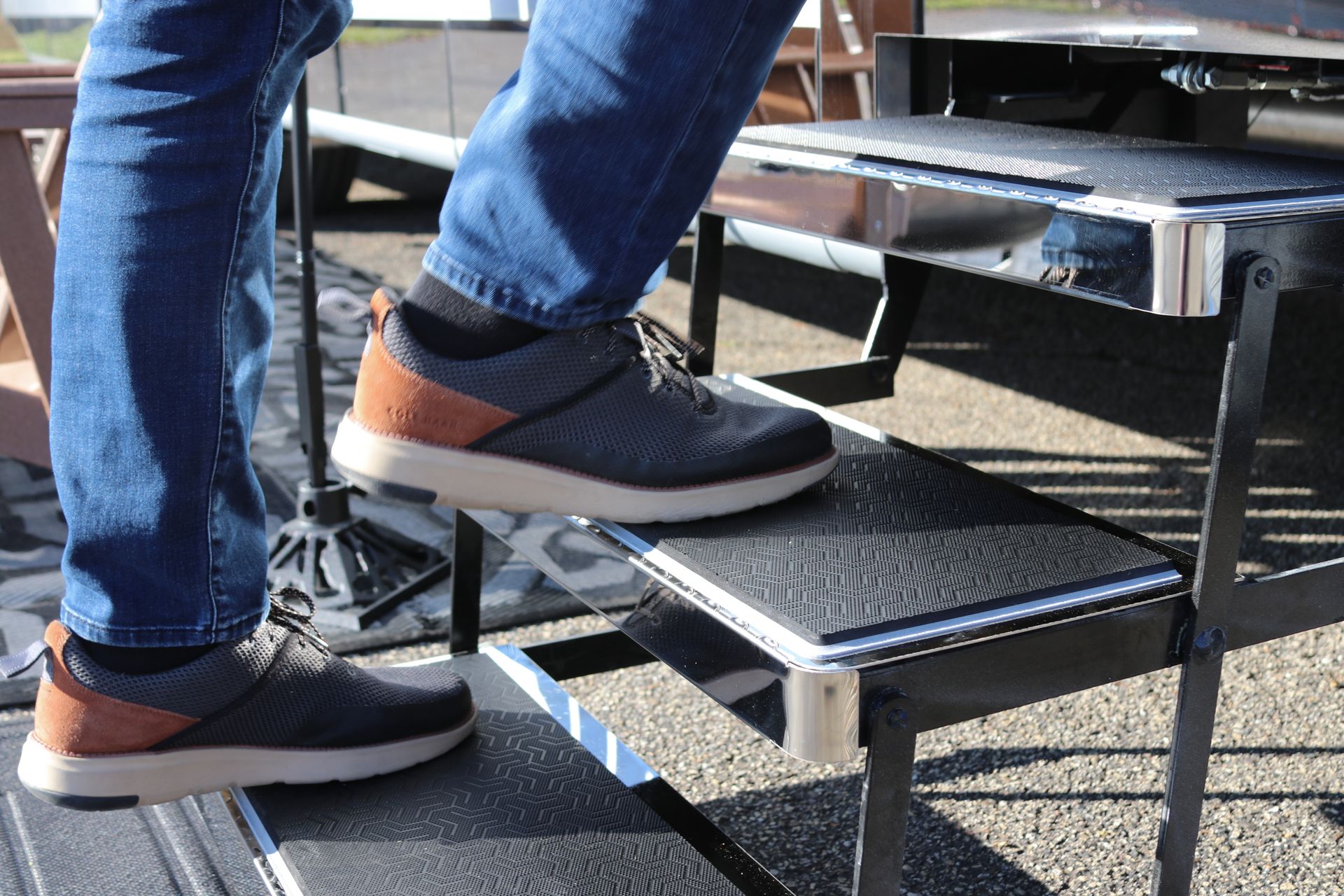 Person's feet on black steps, wearing blue jeans and gray sneakers with brown accents, outside.