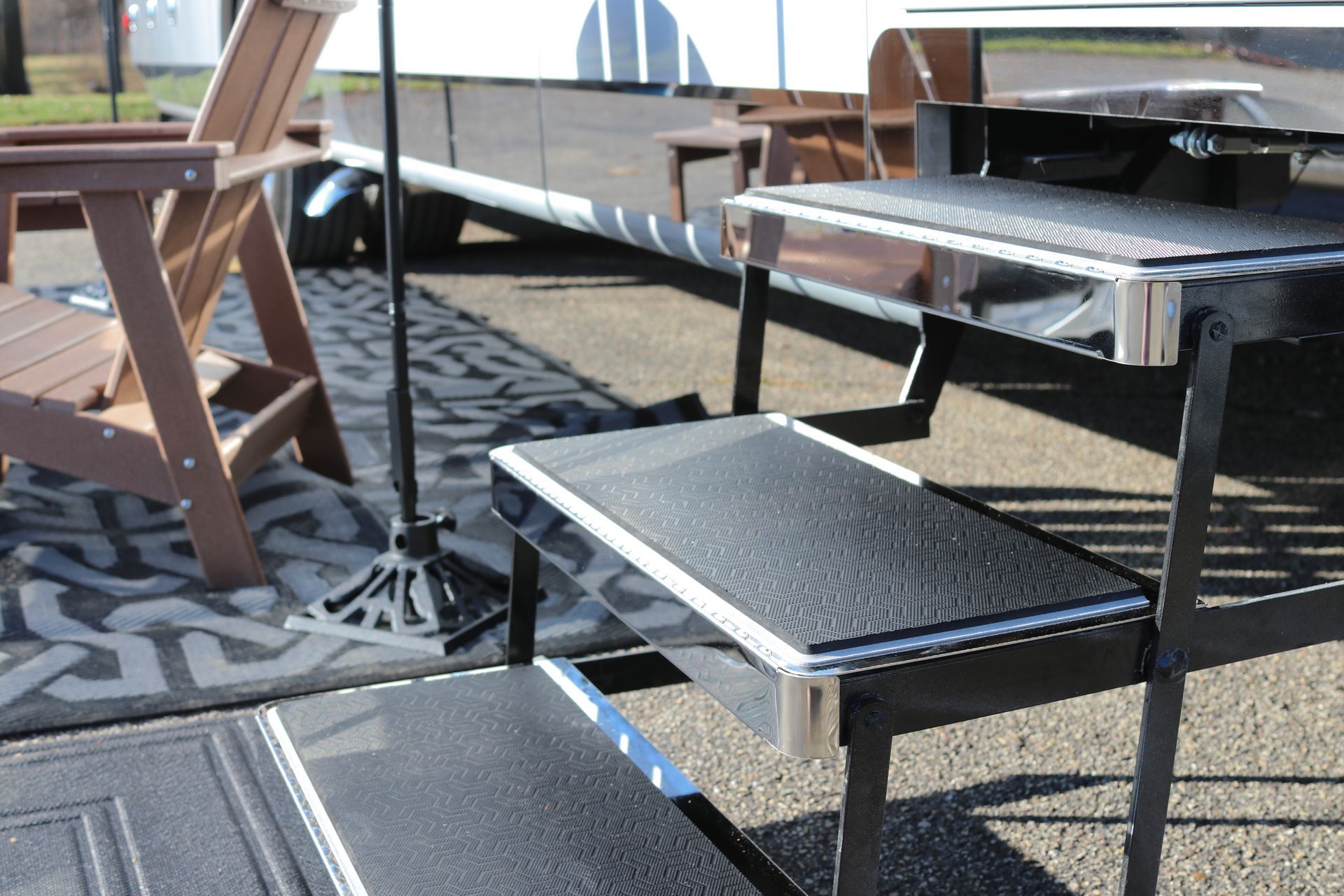 RV steps with black treads and silver trim. Brown folding chair and a rug.