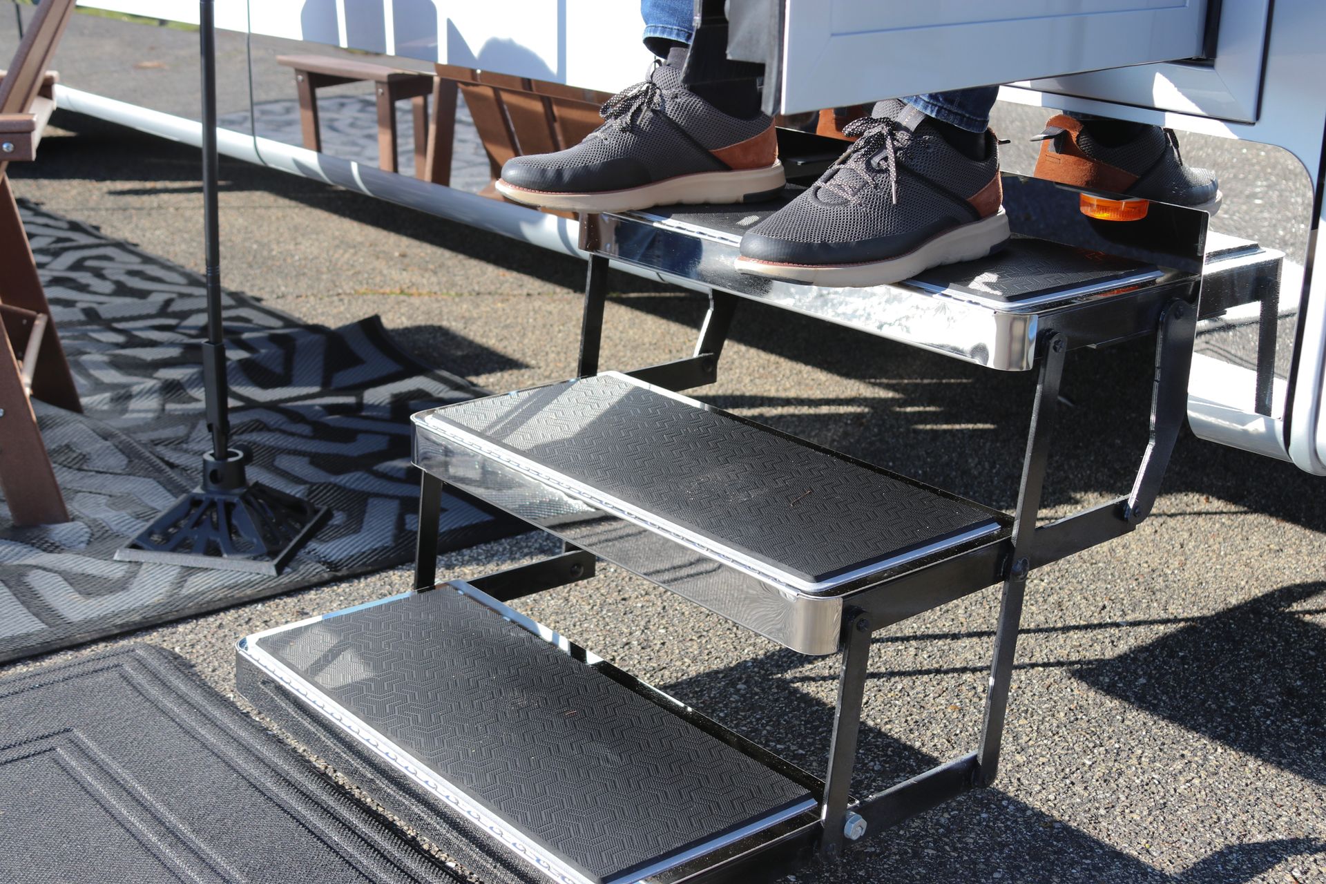 Person's feet on black RV steps. Gray sneakers, black treads, metal frame, outdoor setting.