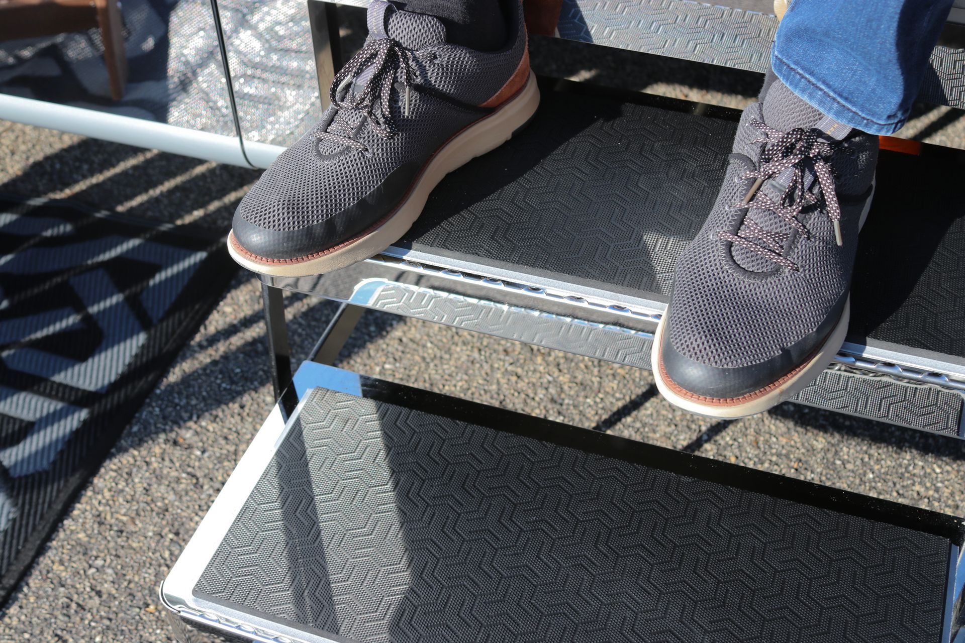 Person's feet on black and silver folding steps. Gray patterned shoes with brown soles.