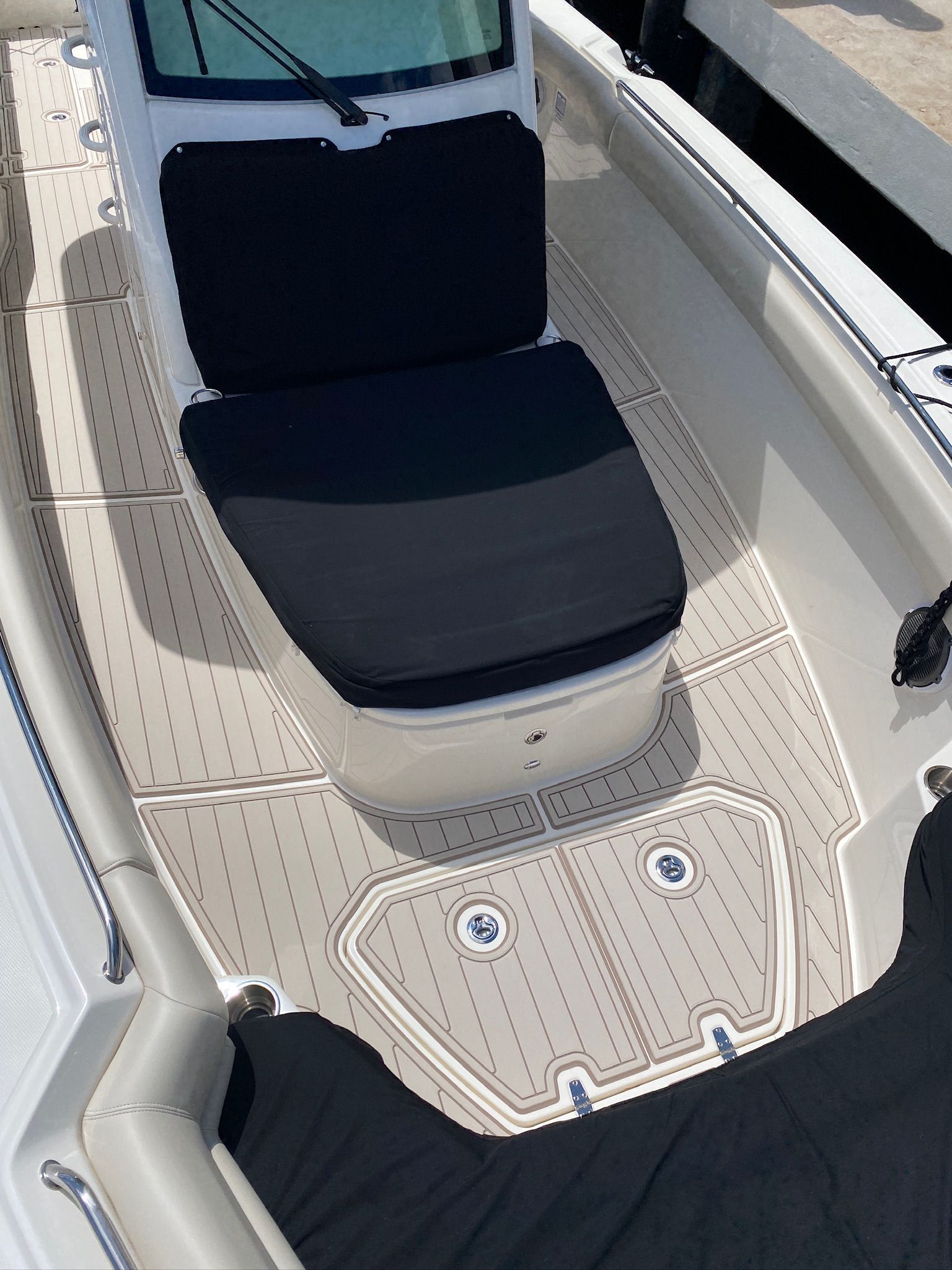 Boat interior with tan flooring, black seating, and covered areas.