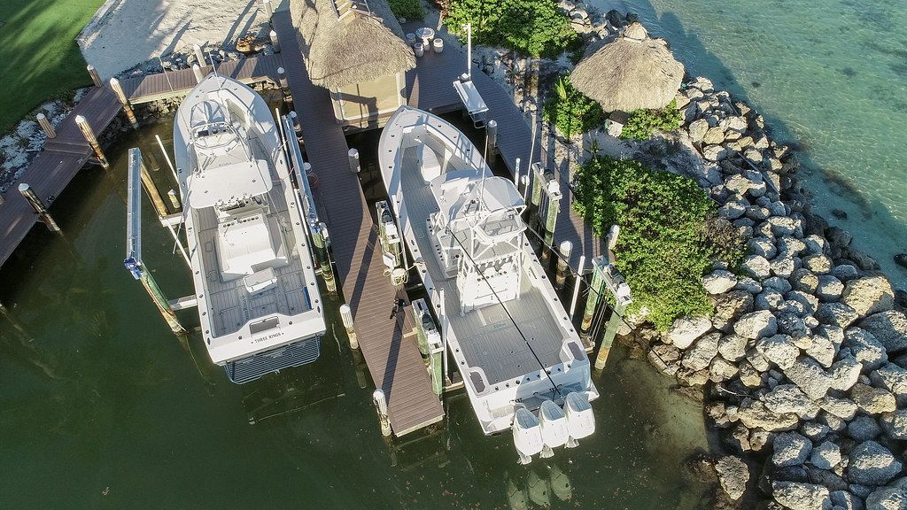 Two white fishing boats docked at a marina with thatched roofs, surrounded by rocks and water.