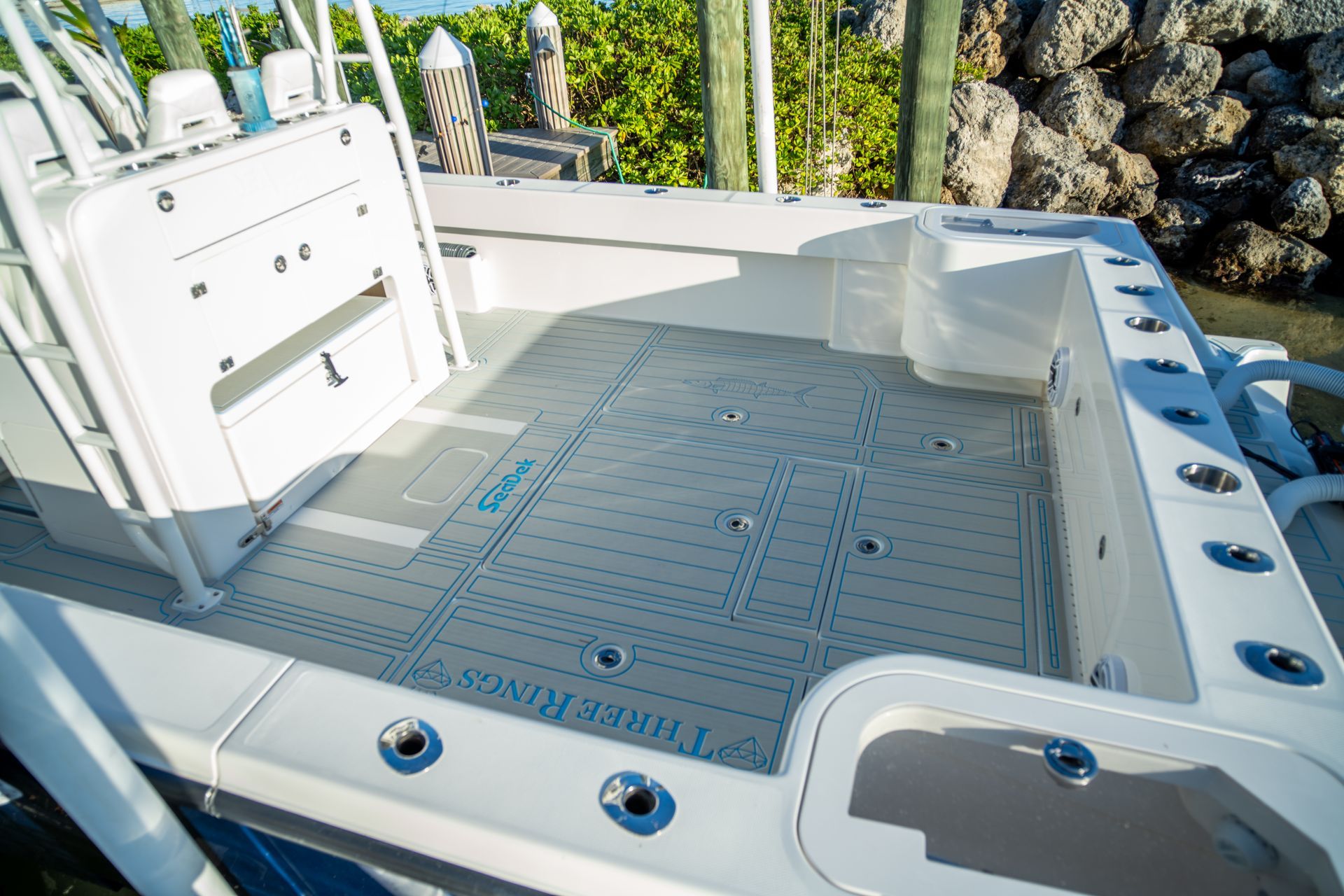 Boat deck with gray and blue flooring, fishing rod holders, and a white seat.