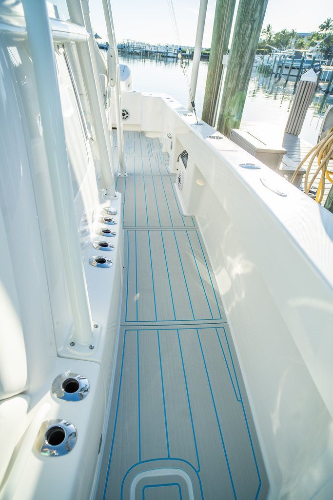 Boat deck with white surface, blue trim, and fishing rod holders along the side.