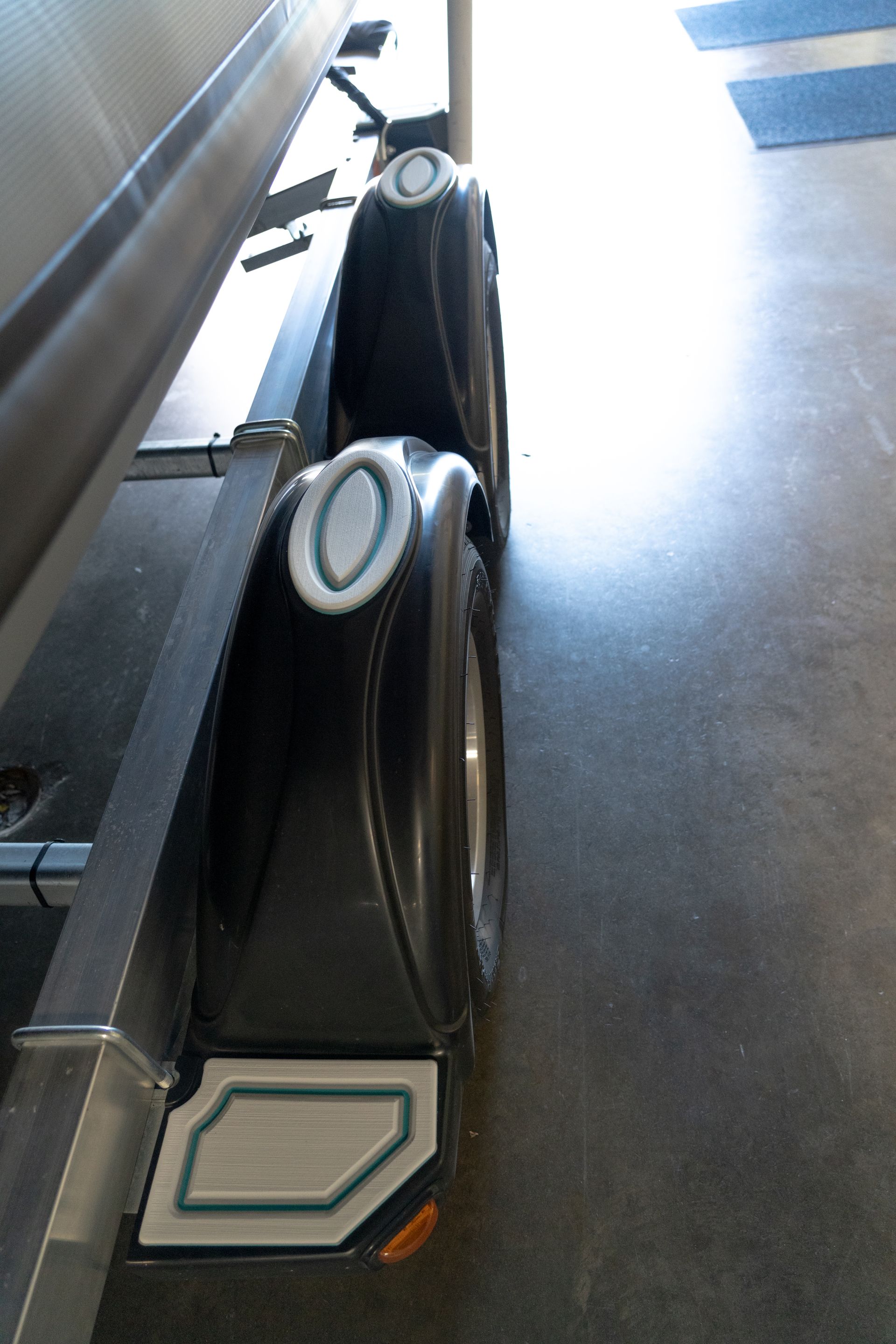 Black boat trailer with two wheels and fenders, parked indoors.