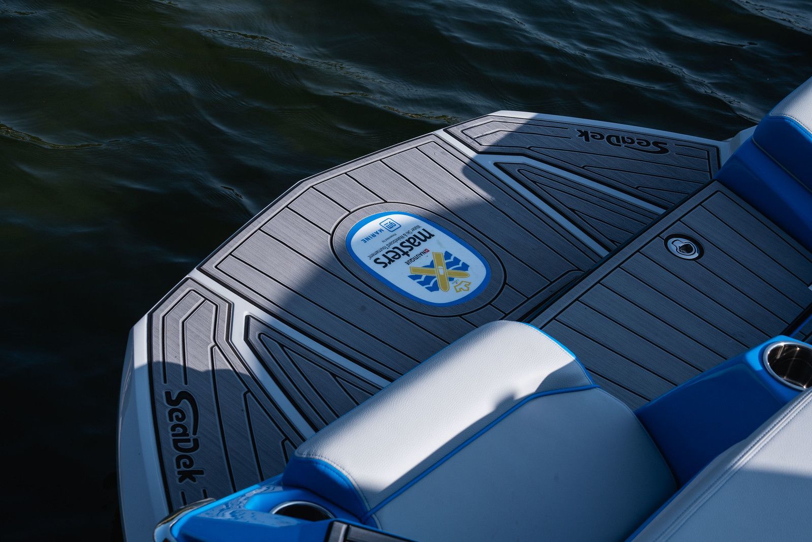 Boat stern with gray SeaDek flooring, blue accents, and a logo over water.