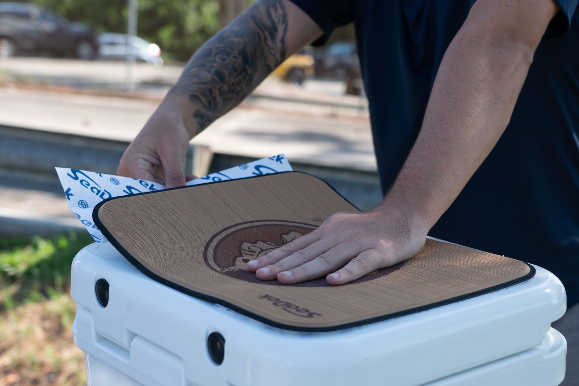 Person placing a mat with a logo on top of a cooler.