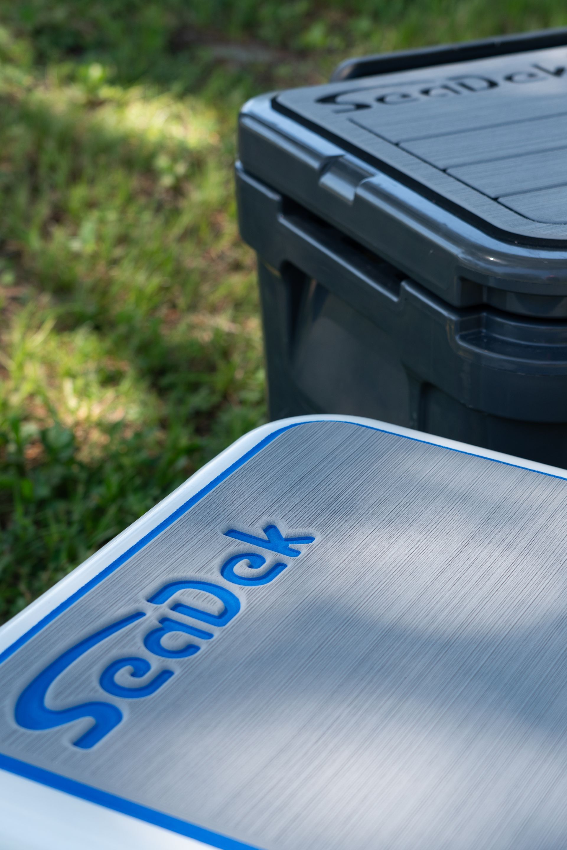 SeaDek cooler and surface outdoors, with the SeaDek logo in blue. A second, darker cooler is behind.