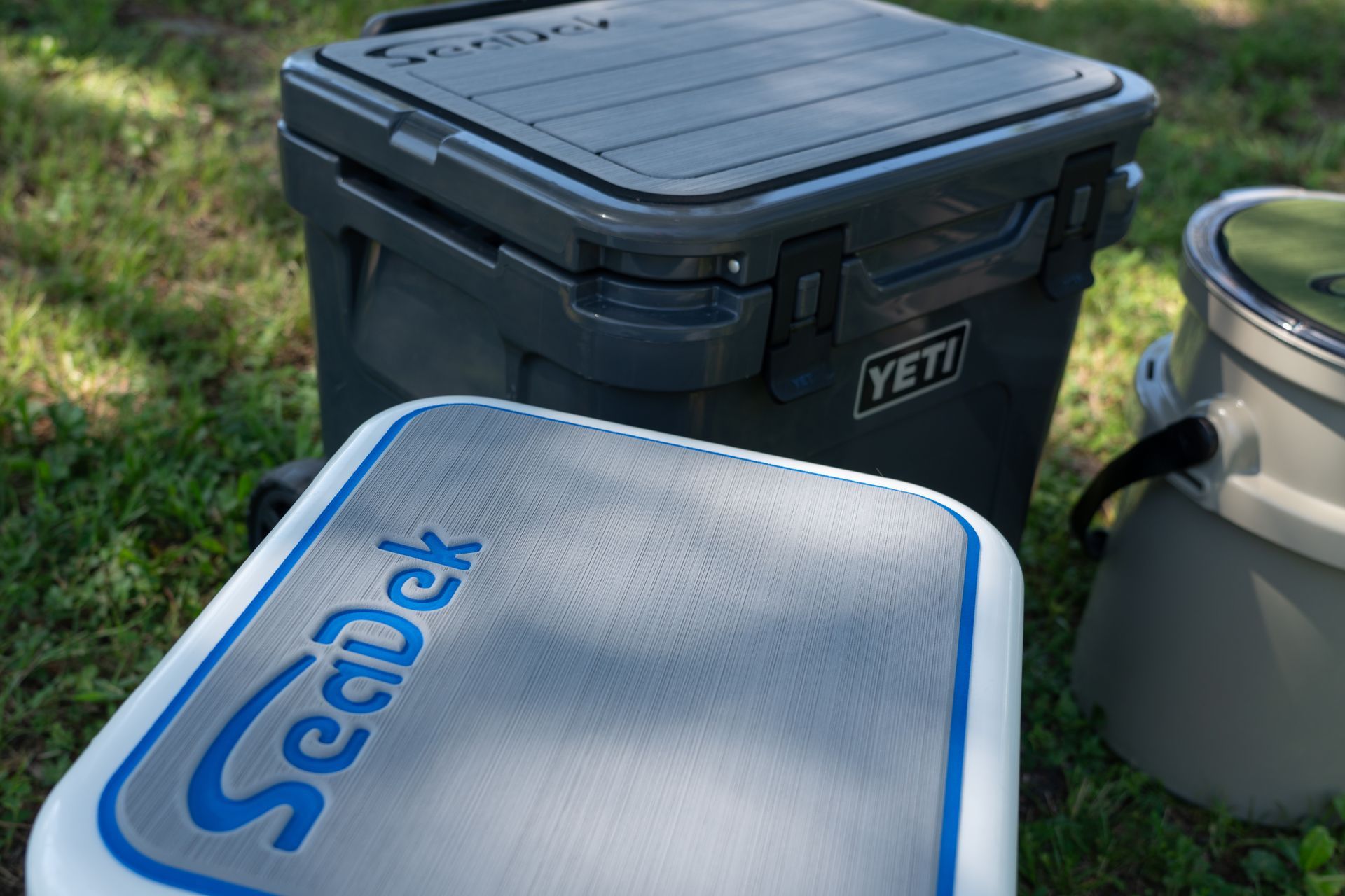 Gray Yeti cooler next to a SeaDek pad and a smaller green container, outdoors.
