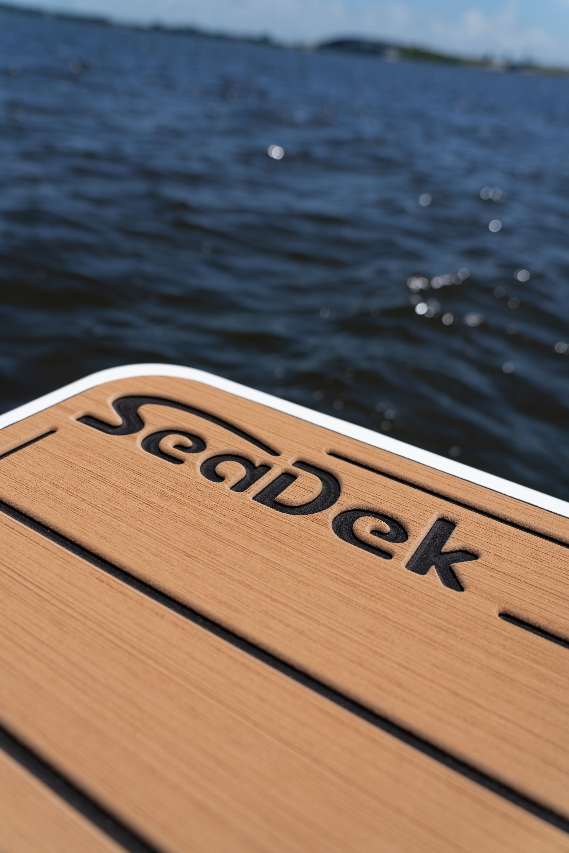 SeaDek logo on a brown boat deck, with a dark blue ocean in the background.
