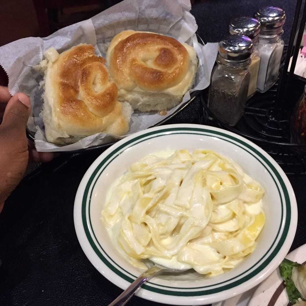a bowl of pasta next to a basket of rolls