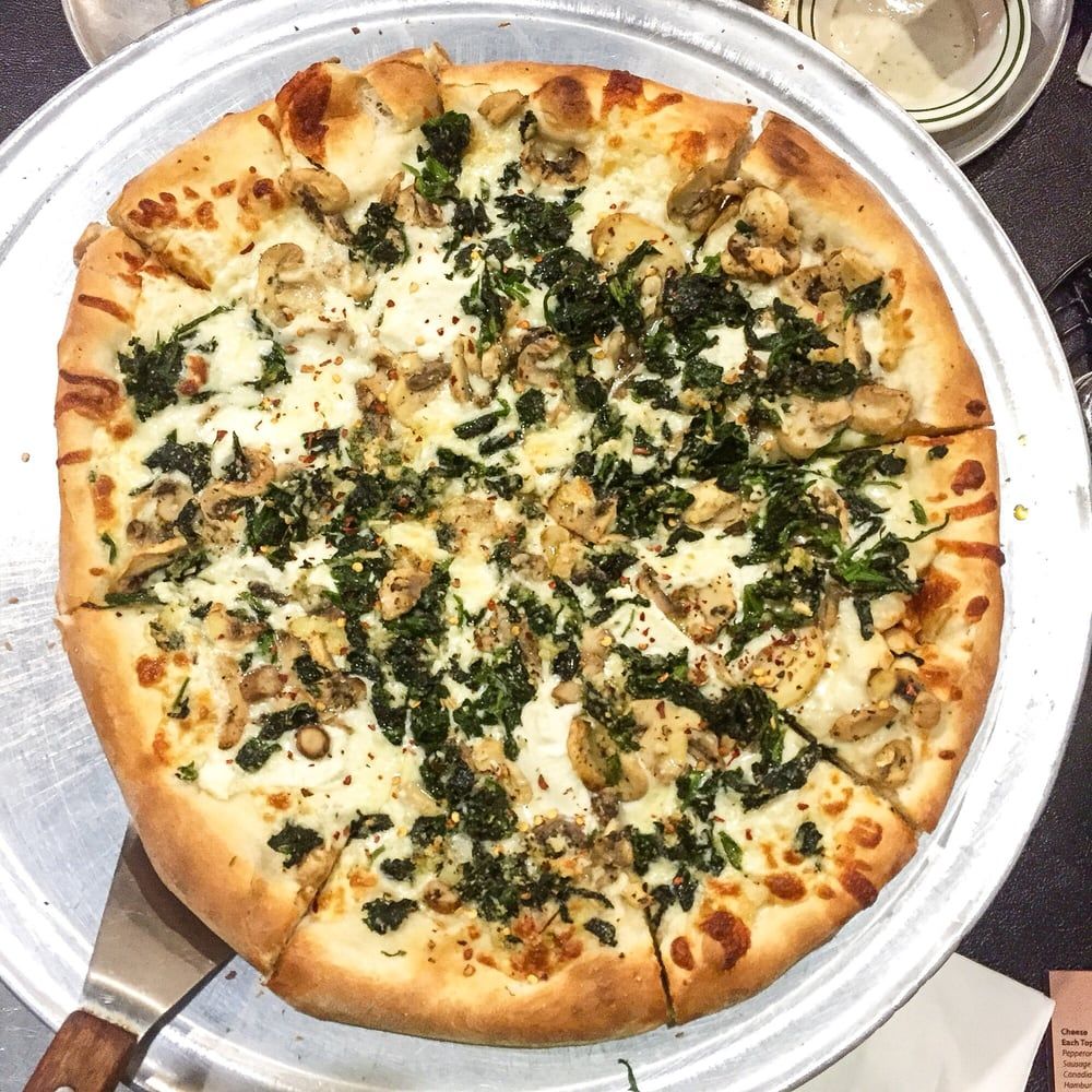 a pizza with spinach and mushrooms on it is on a pan