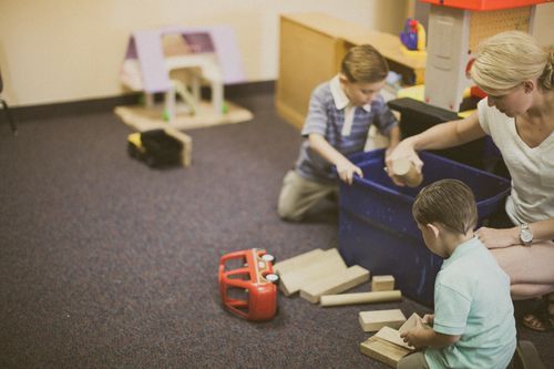 Two children and an adult sorting toys in a play area.