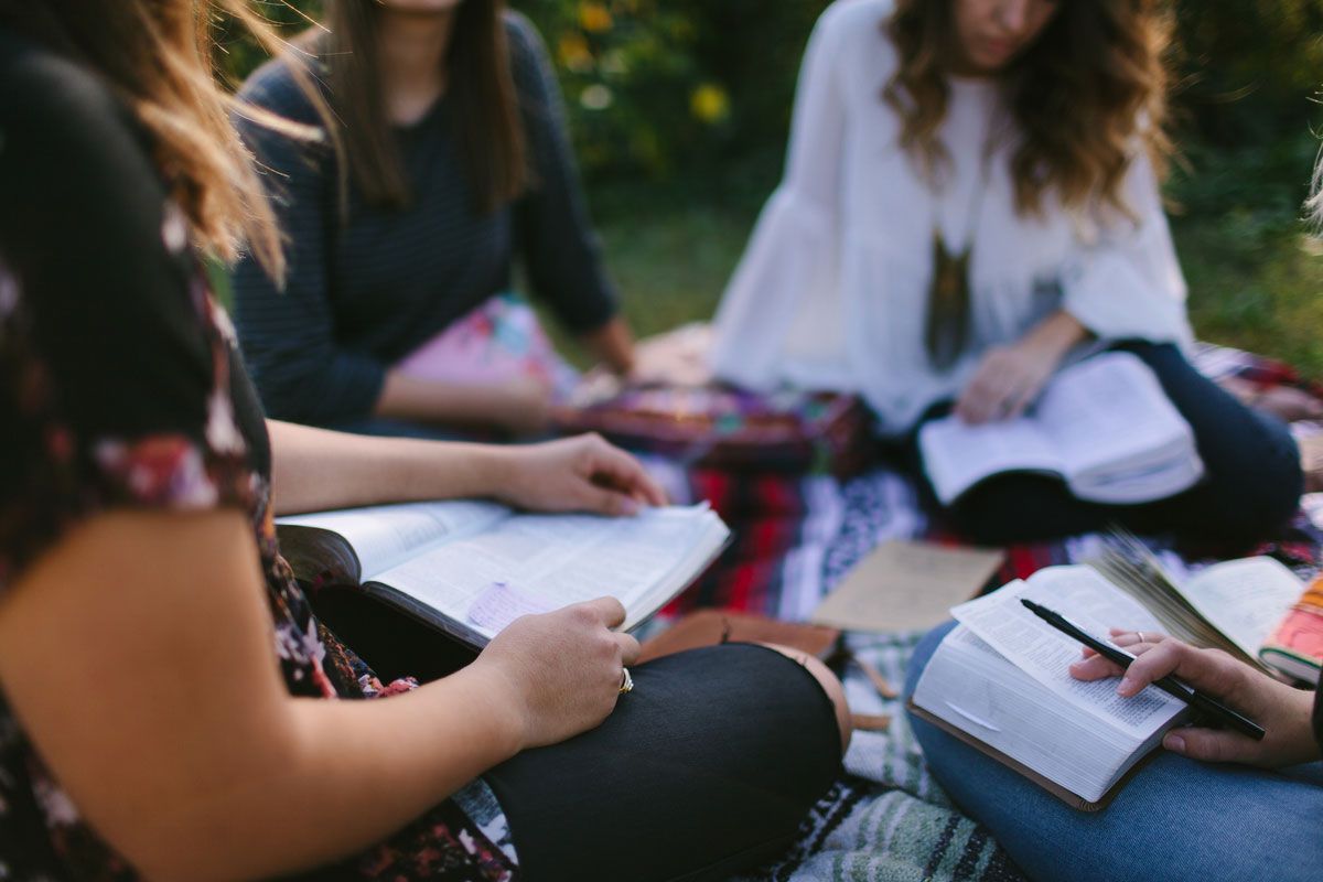 Four people sitting on a blanket outdoors, reading and writing in books.