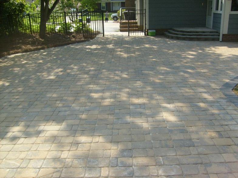 A brick driveway leading to a house with a fence