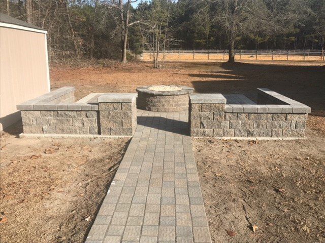 A brick walkway leading to a fire pit in a backyard.