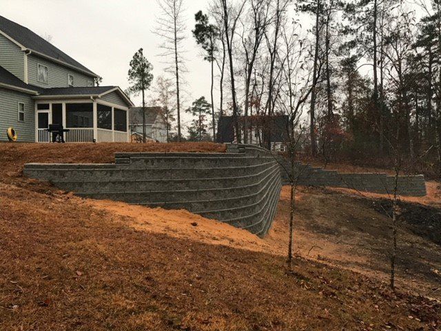 A house with a screened in porch is sitting on top of a hill next to a retaining wall.
