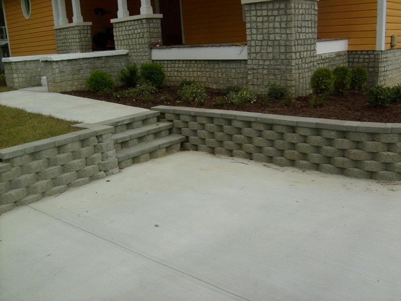 A brick wall surrounds a concrete driveway in front of a house.