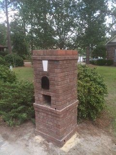 A brick chimney is sitting in the middle of a yard.
