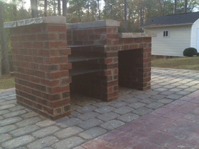 A brick bench is sitting on a patio in front of a house.