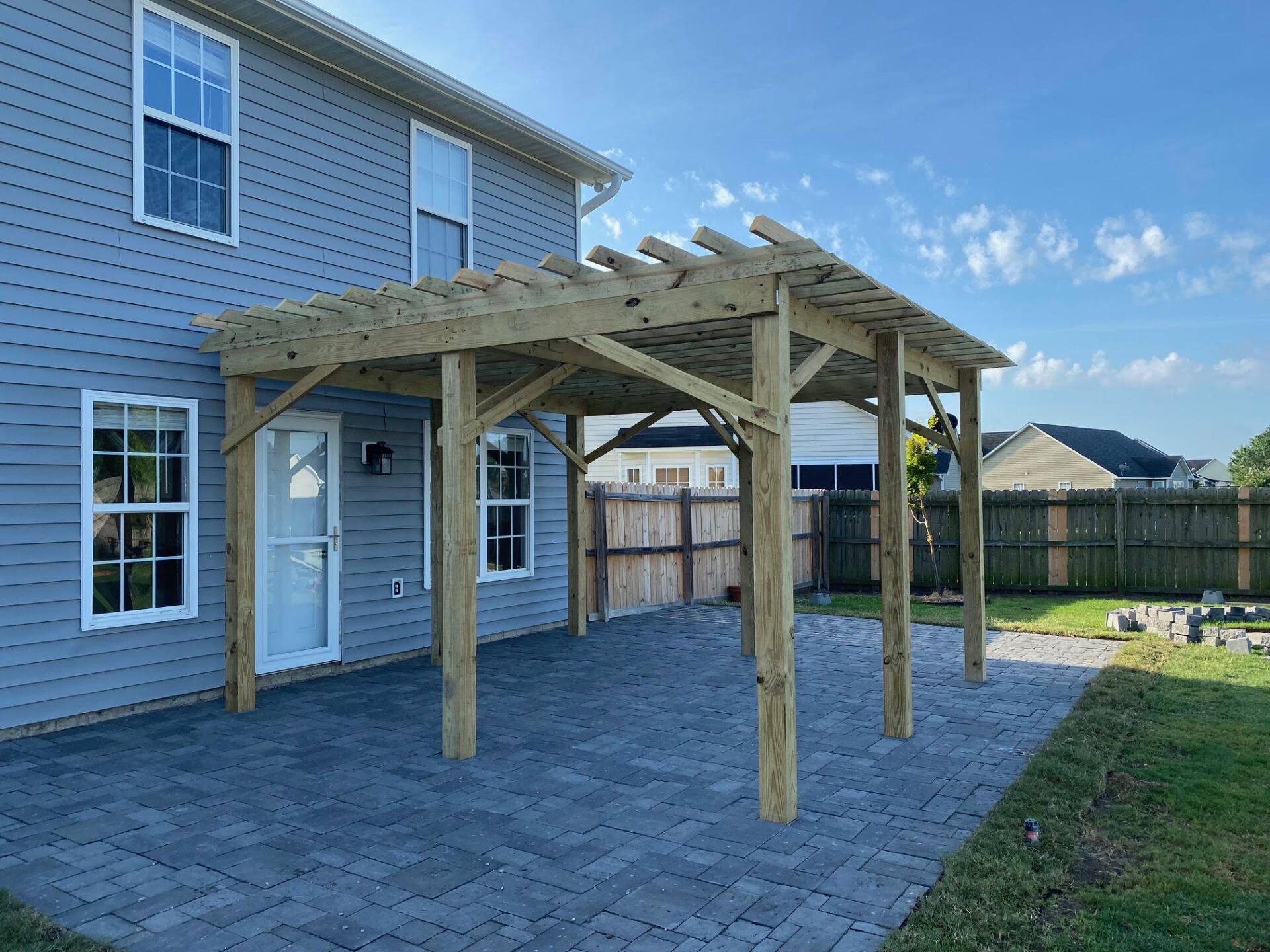 A wooden pergola is sitting in the backyard of a house.