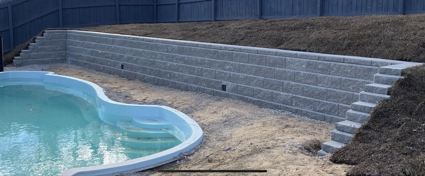 A swimming pool is surrounded by a stone wall in a backyard.