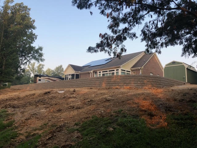 A house with solar panels on the roof is sitting on top of a dirt hill