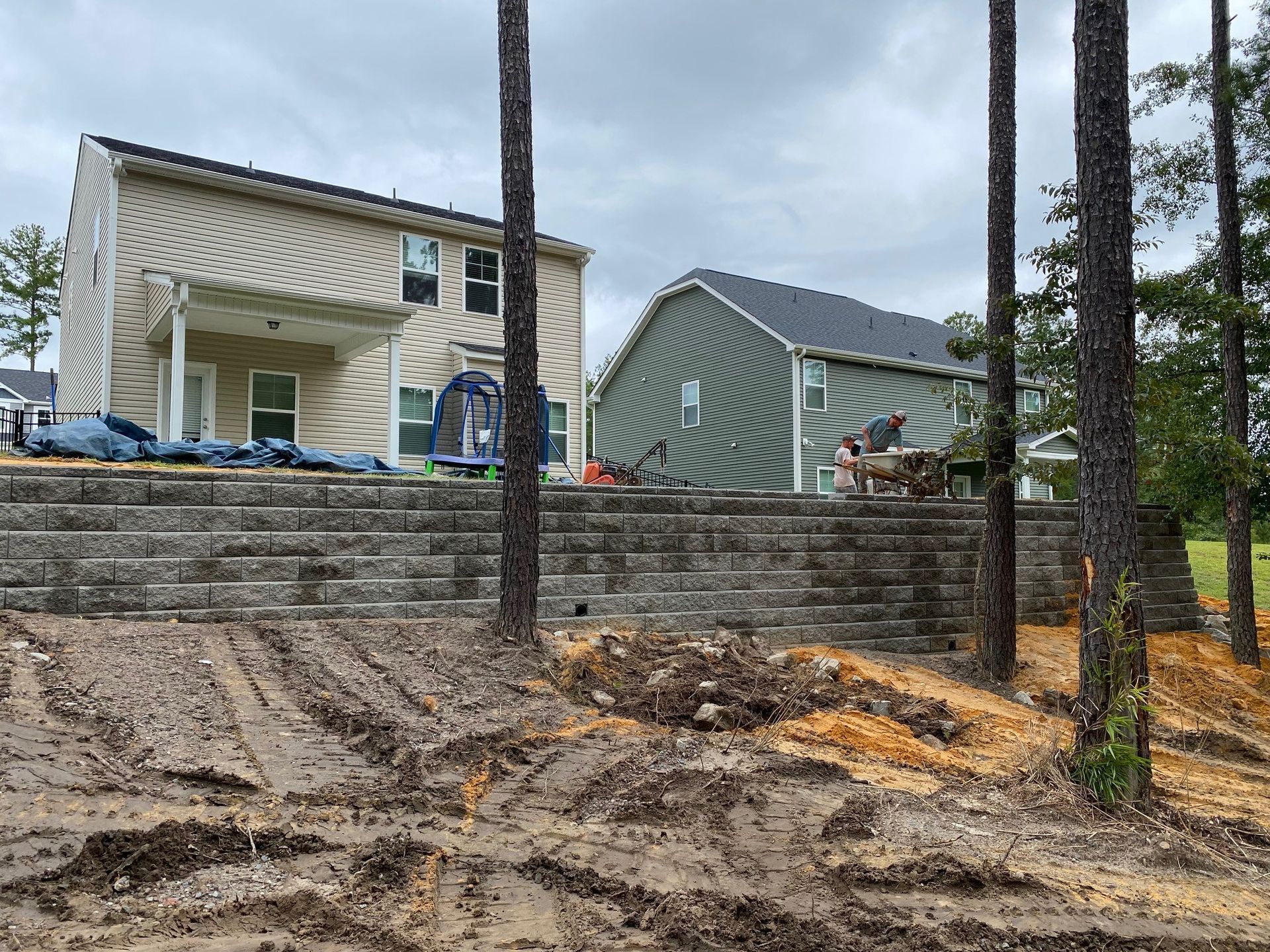 A house is being built next to a retaining wall surrounded by trees.