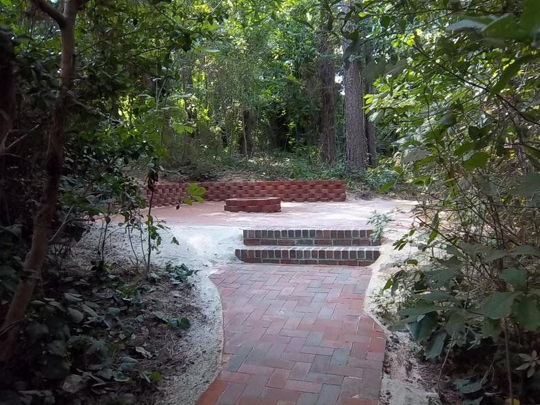 A brick walkway leading to a patio in the middle of a forest.