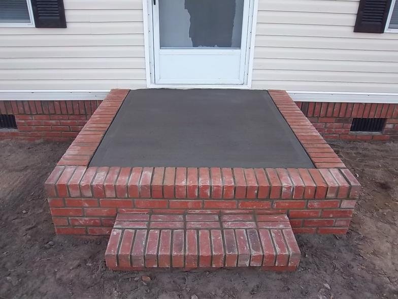 A brick porch with a concrete step in front of a house.