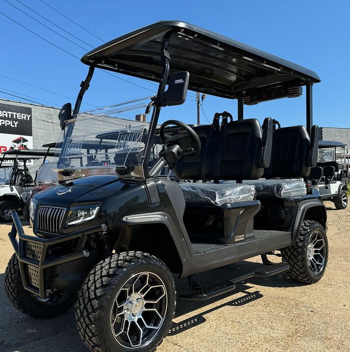 A black golf cart is parked in a dirt field.