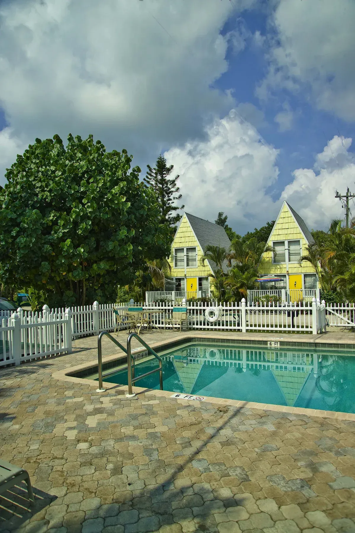 A swimming pool in front of a yellow house with a white fence