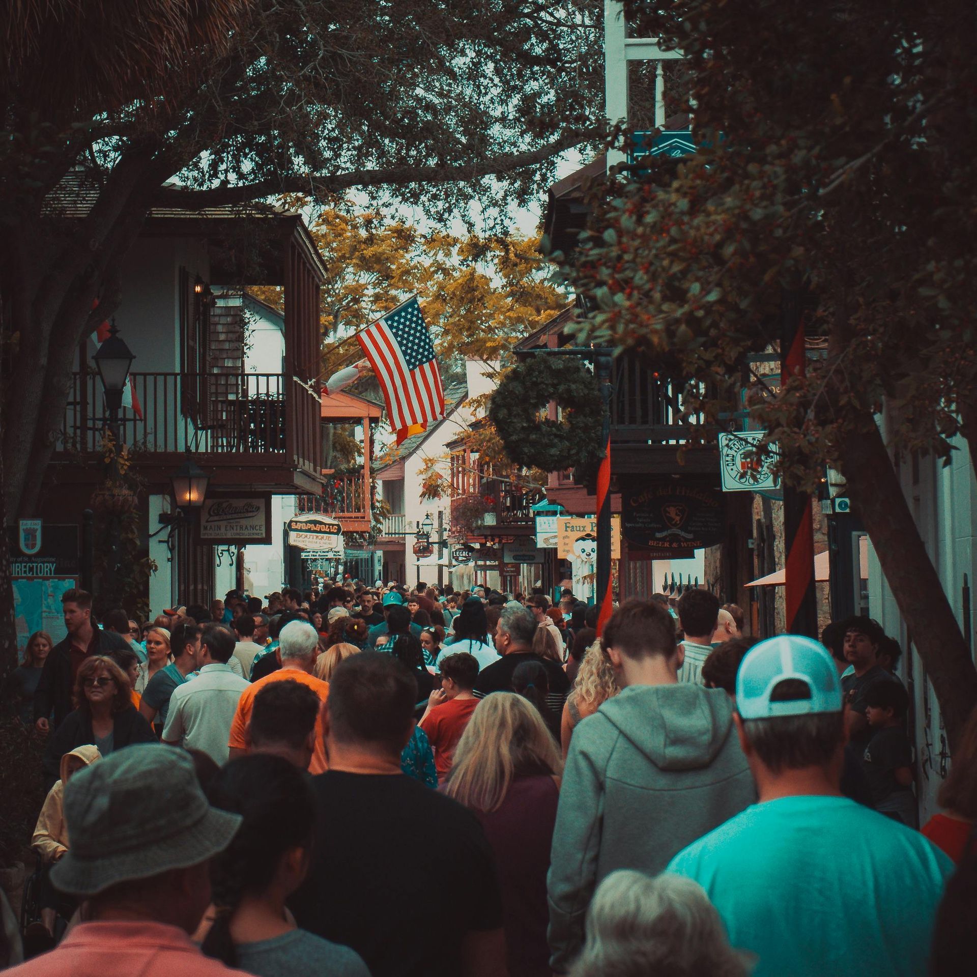 A crowd of people walking down a street with an american flag in the background