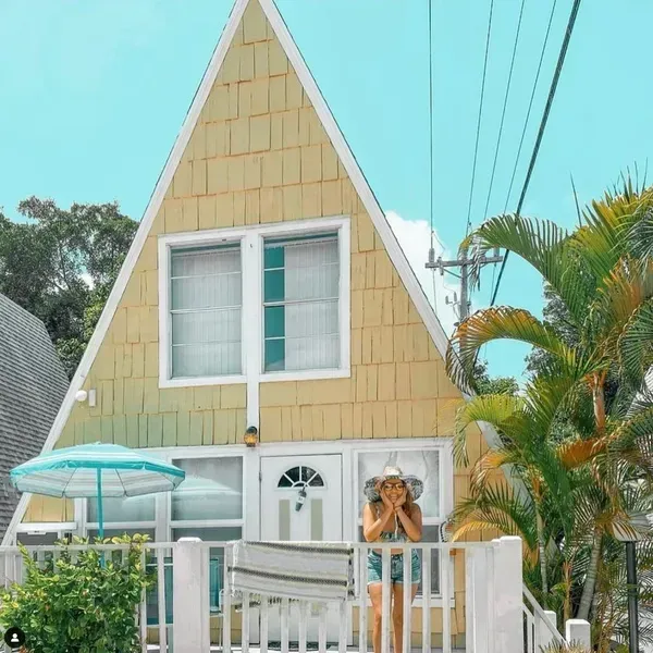 A woman is standing in front of a yellow a frame house.
