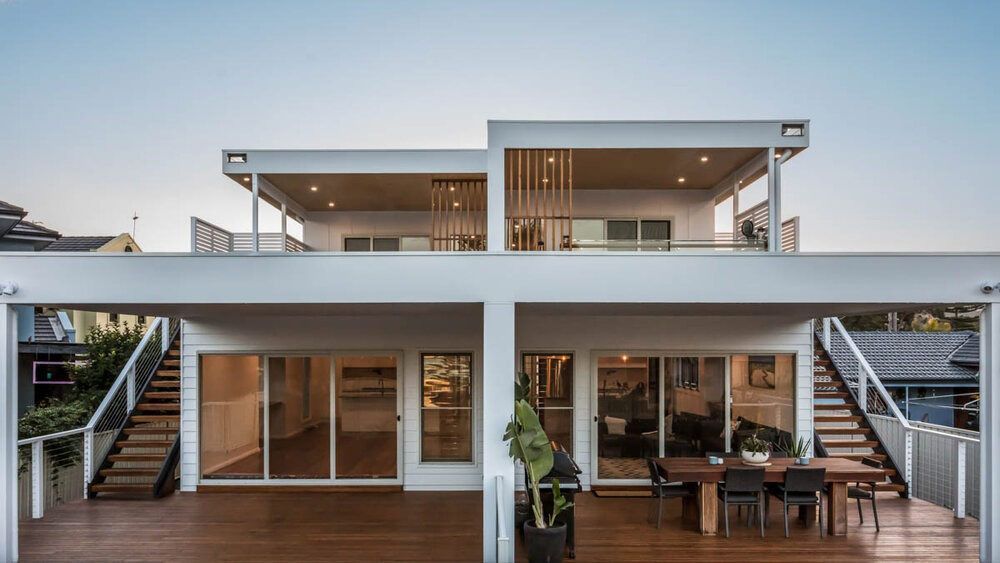 A Large White House With a Wooden Deck and Stairs Leading Up to It — DeBu Studios In Russell Vale, NSW