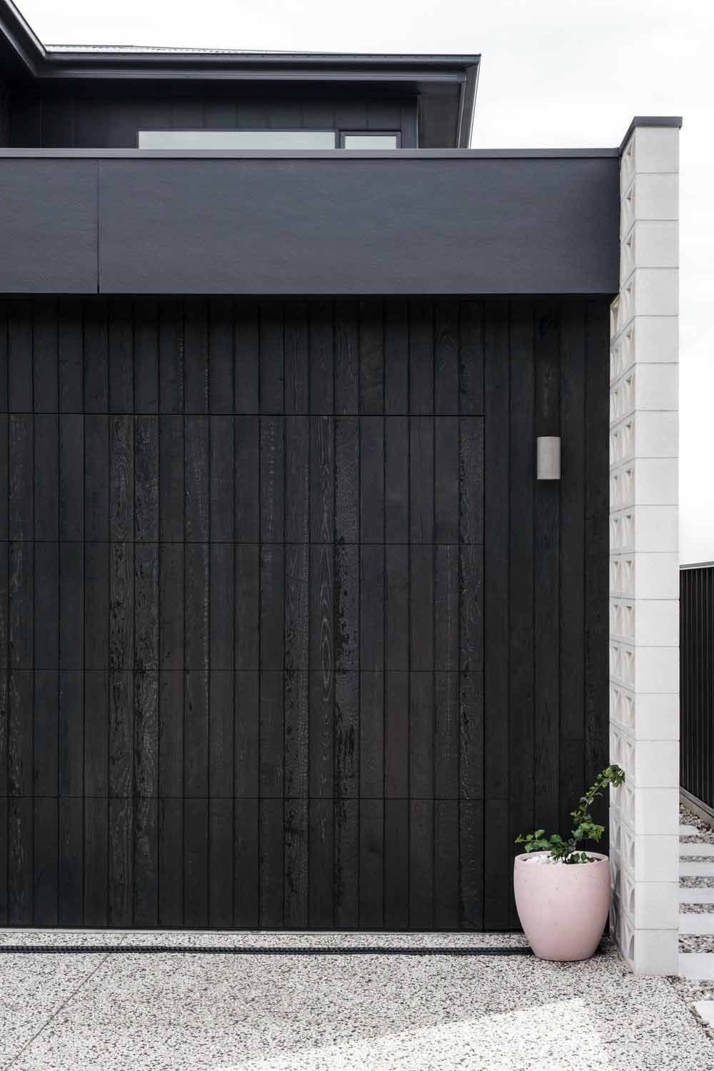 A Black Garage Door With a Pink Potted Plant in Front of It — DeBu Studios In Russell Vale, NSW