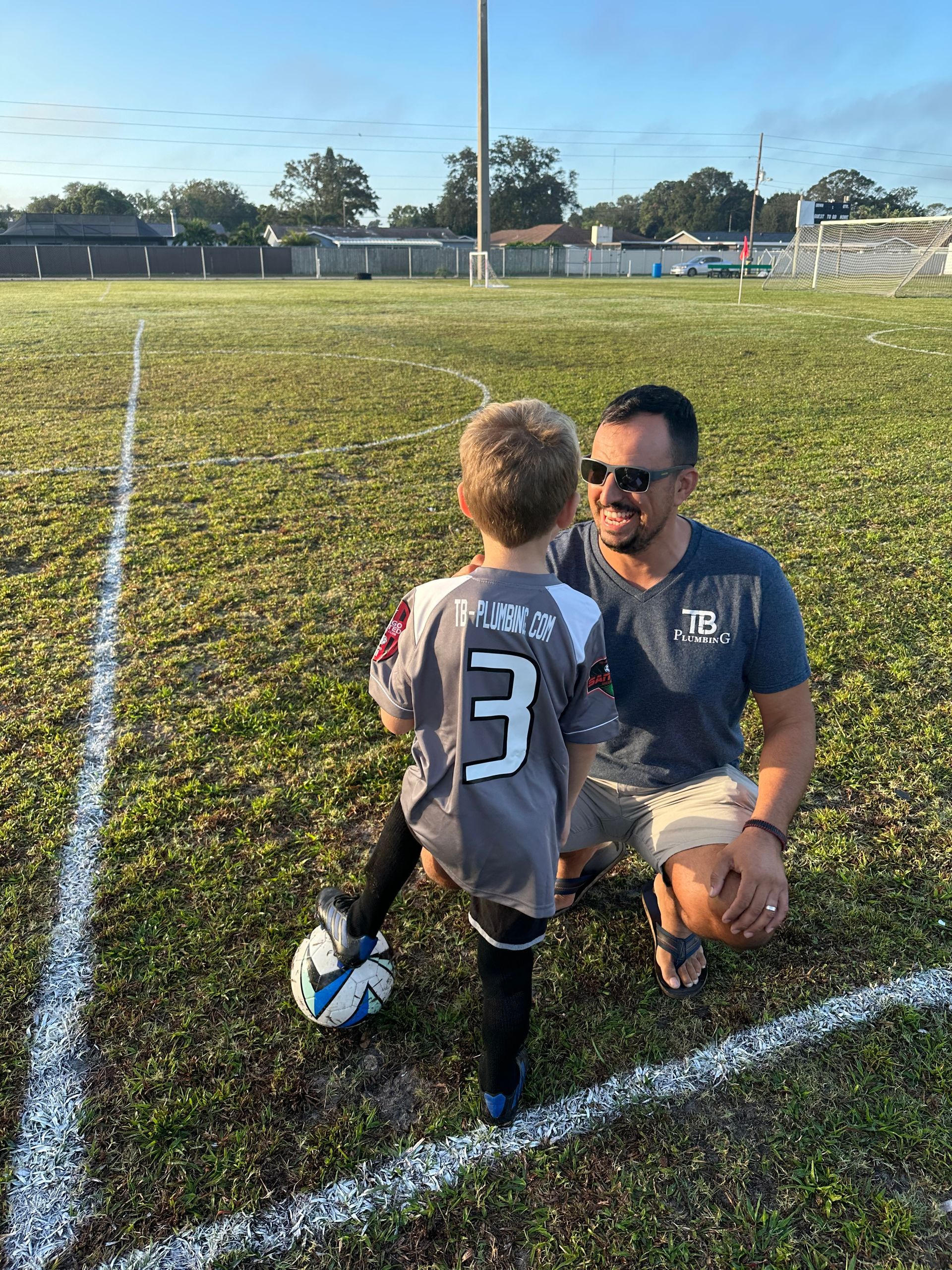 A man is kneeling down next to a little boy on a soccer field.