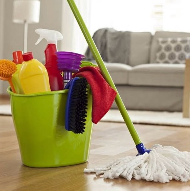 Man in red overalls cleaning a counter with a squeegee, holding a blue bucket.