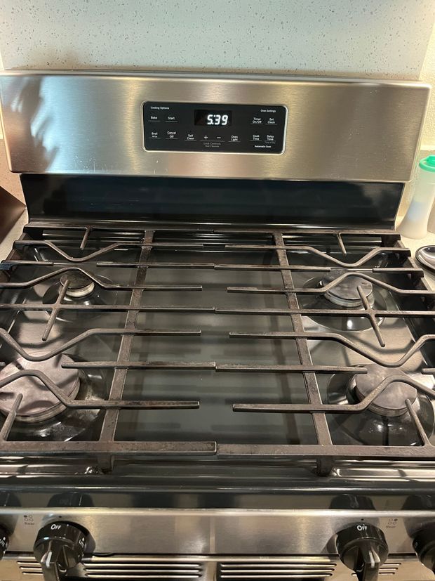 Person wearing gloves cleaning a dirty white stovetop with a blue cloth.