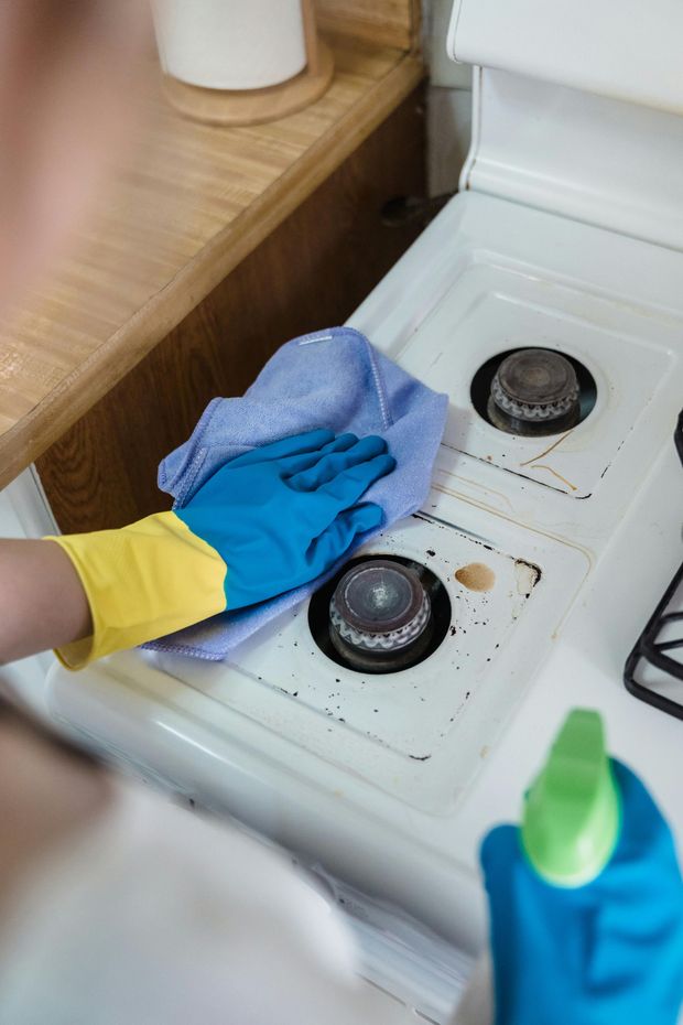 Person wearing gloves cleaning a dirty white stovetop with a blue cloth.