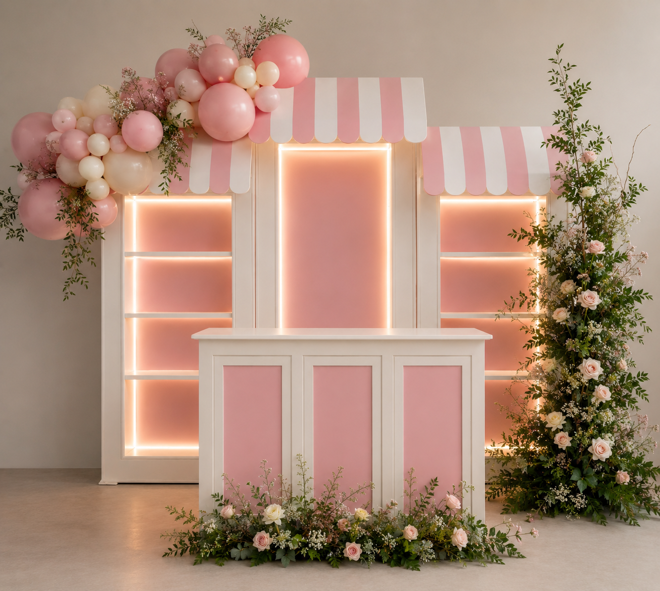 Mesa de doces rosa e branca com balões, painel listrado ao fundo e painéis luminosos, decorada com flores.
