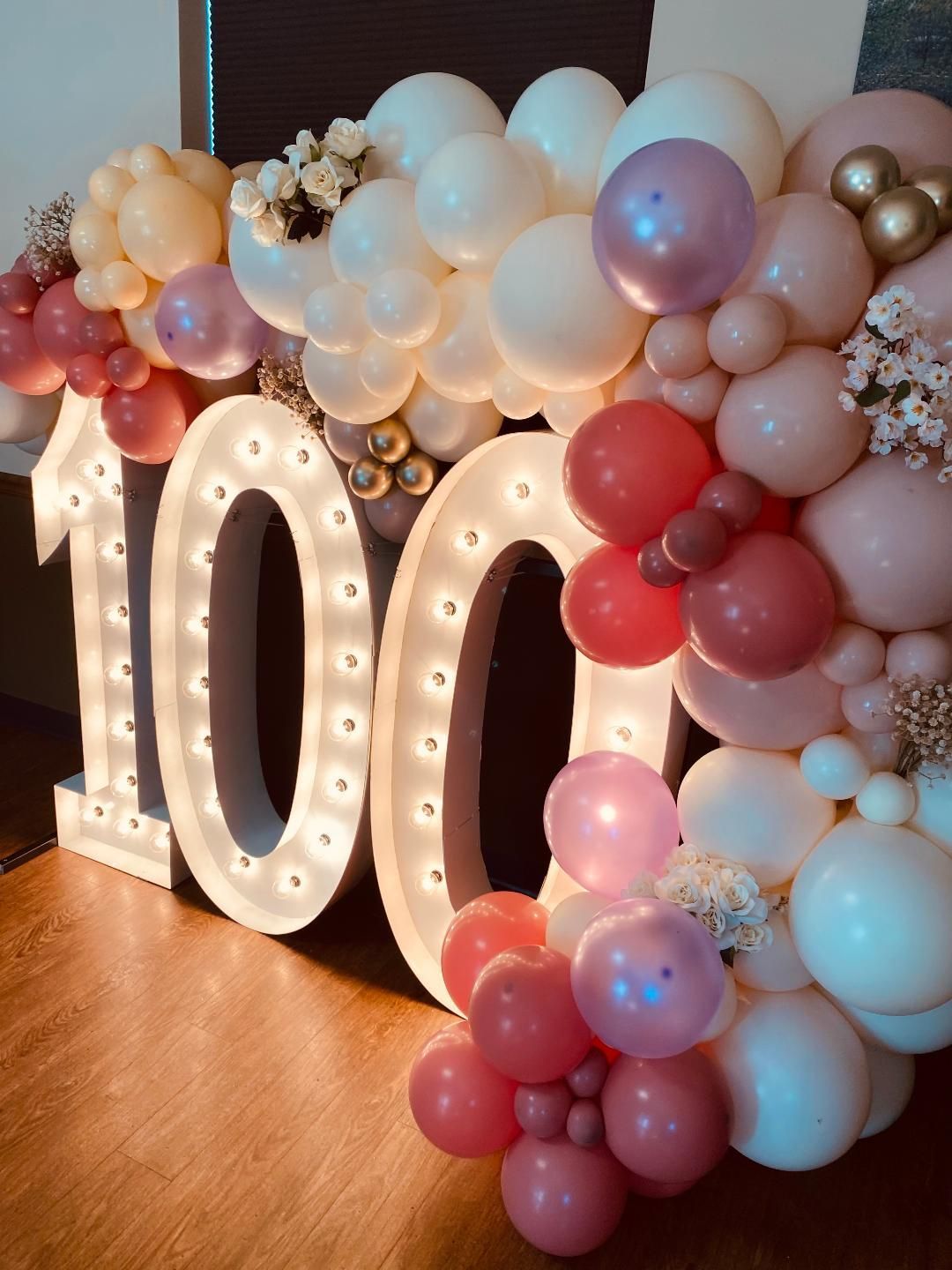 The number 100 is surrounded by pink and white balloons.