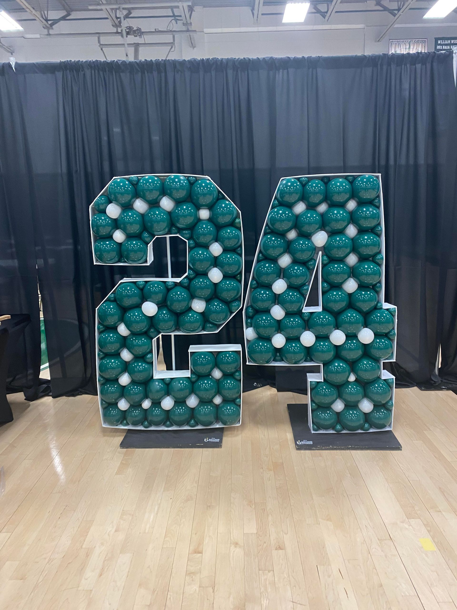 A large number 24 made of balloons is sitting on a wooden floor.