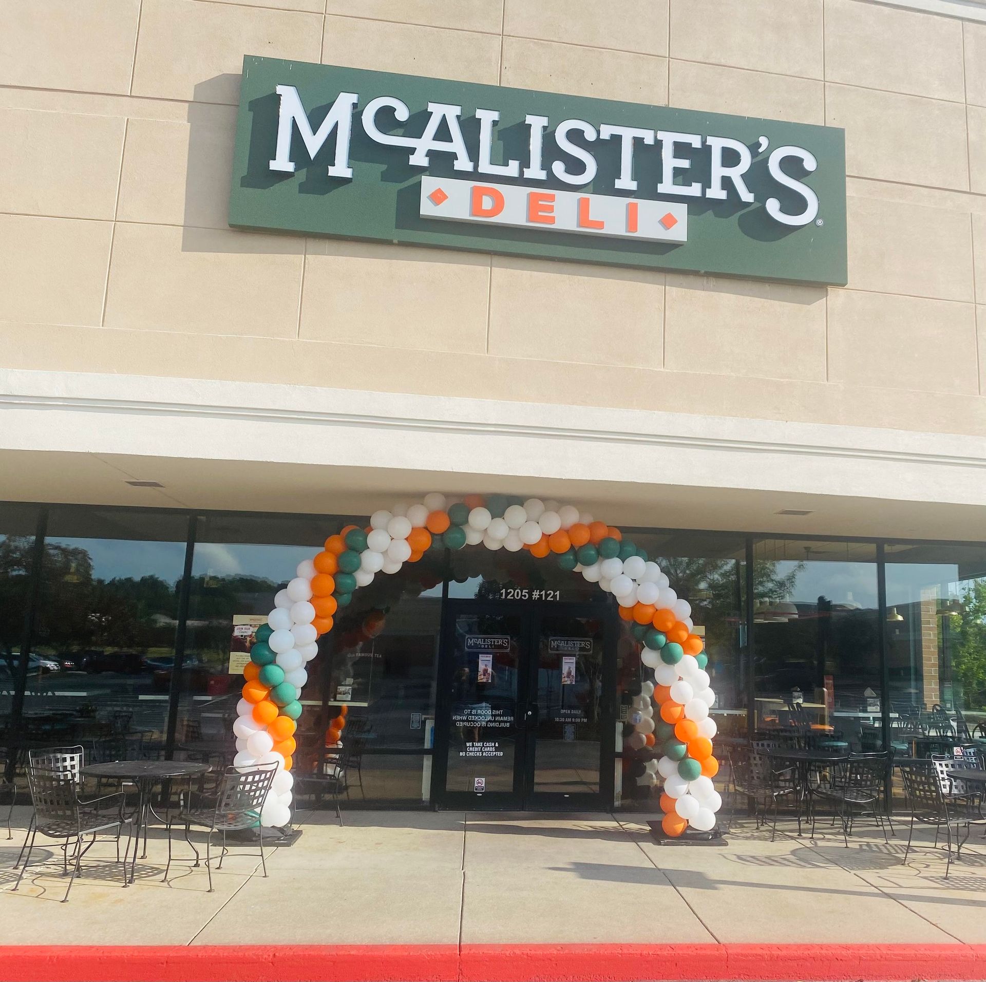 McAlister's Deli storefront with an archway of orange, white, and green balloons.
