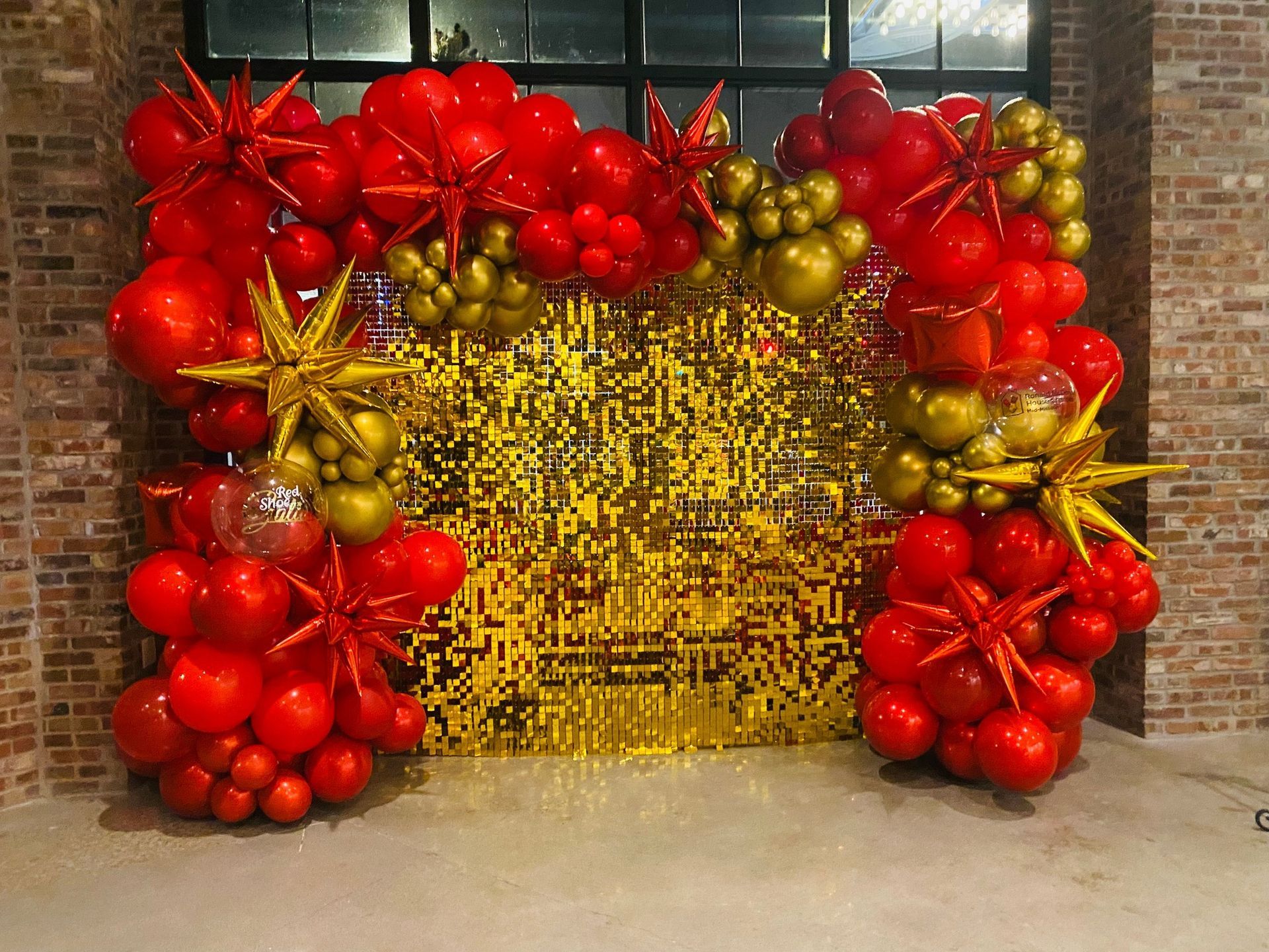 Red and gold balloon arch framing a gold fringe backdrop; indoors.