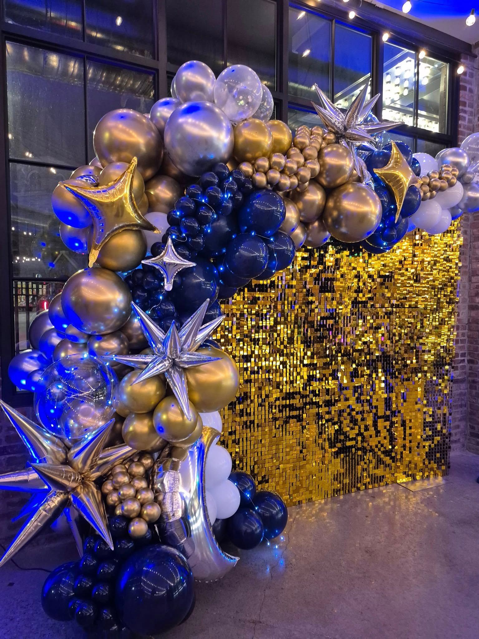 Balloon arch with gold, silver, and blue balloons, and a gold sequin wall backdrop.