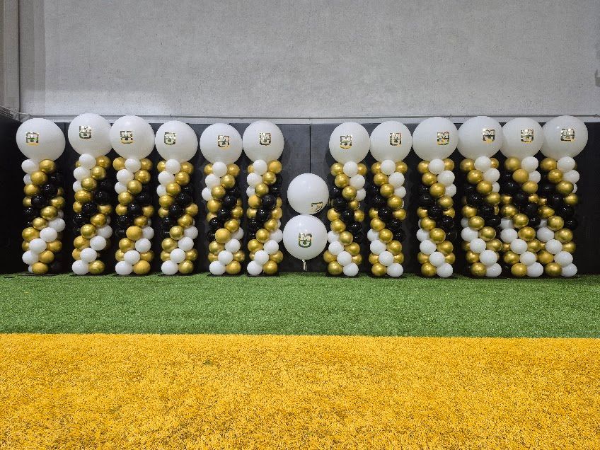 Balloon columns in black, gold, and white with numbers on top, set on green turf.