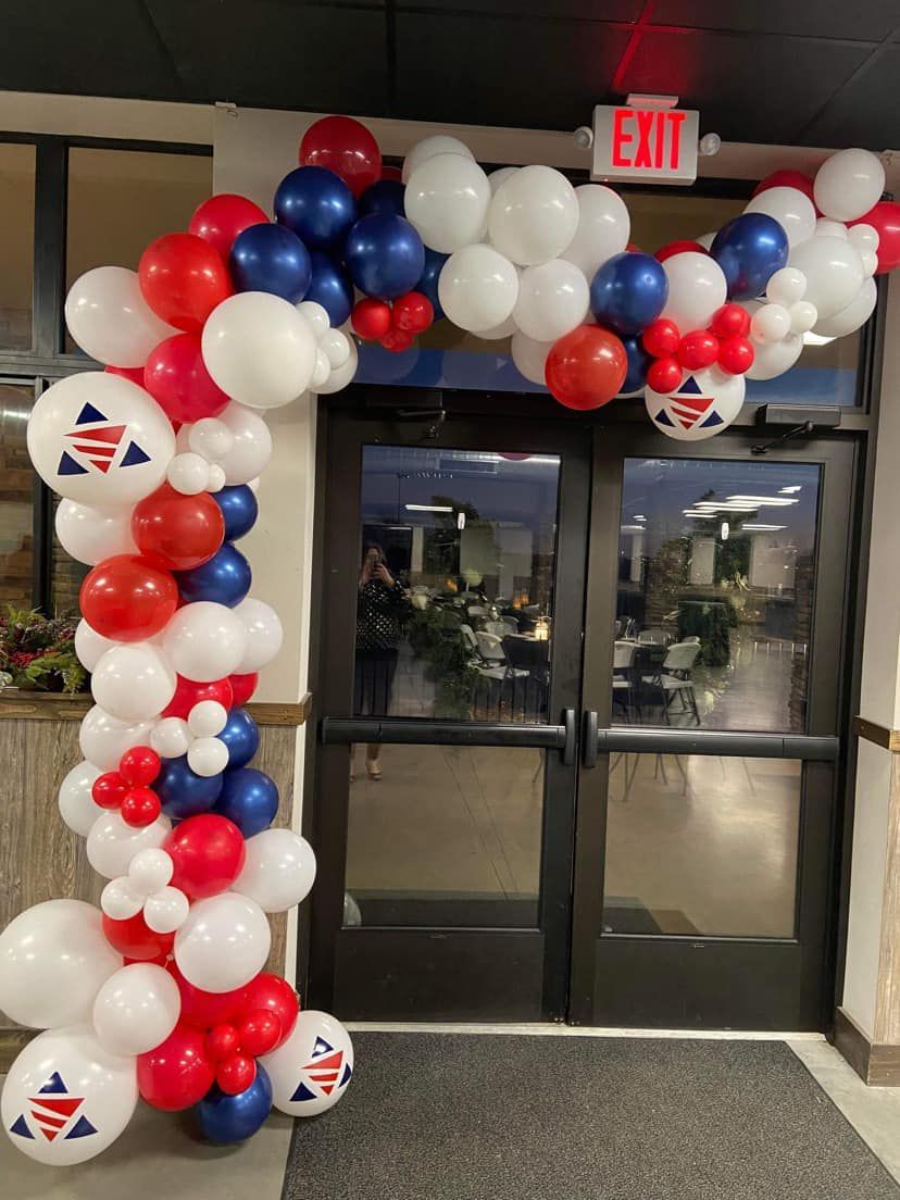 A red , white and blue balloon arch is in front of a door.
