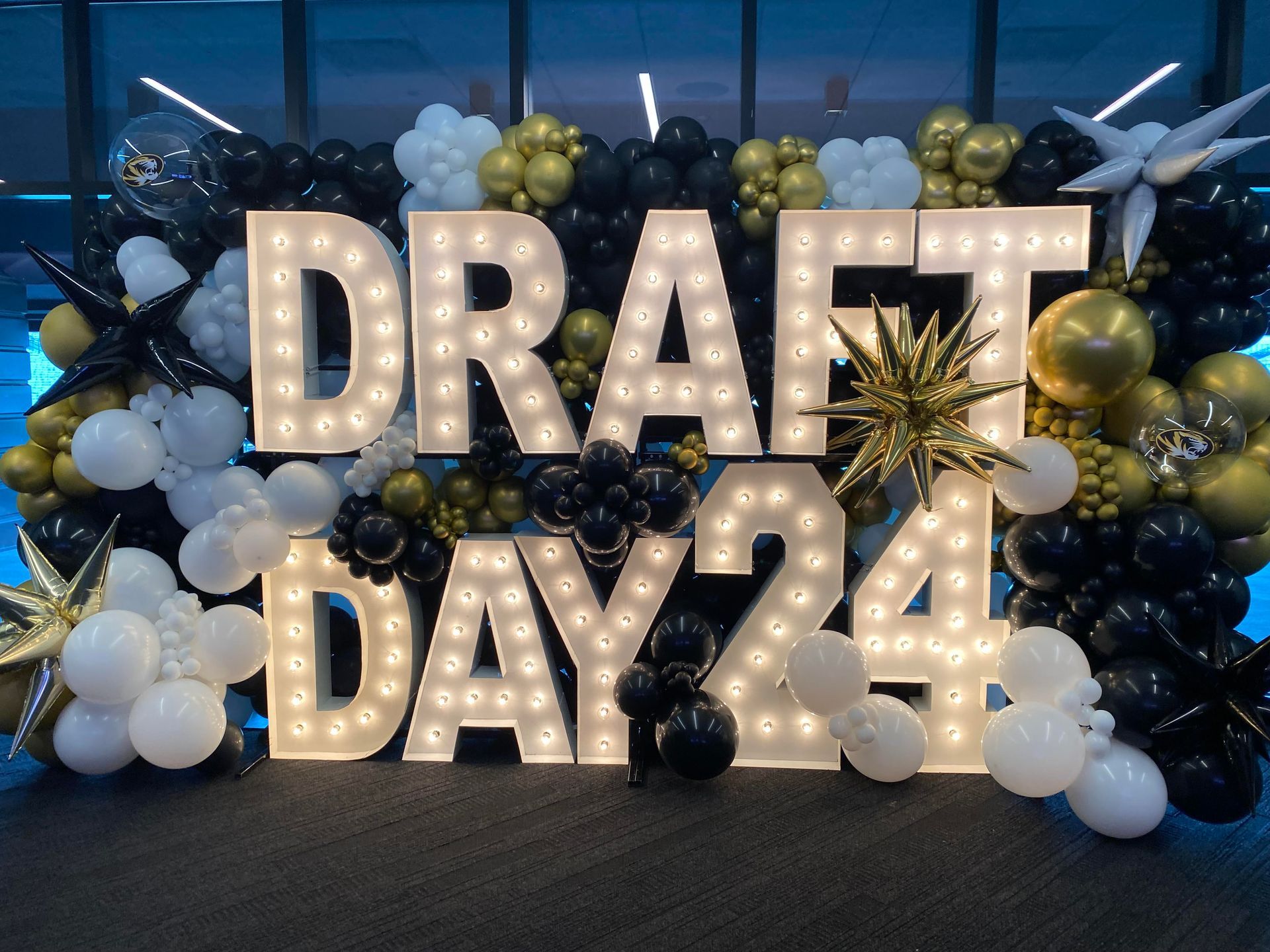 A sign that says draft day 24 is surrounded by balloons and lights.